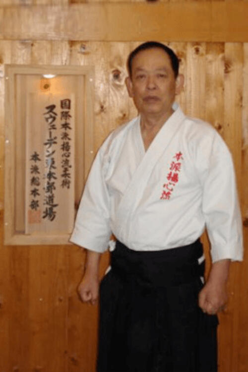 Soke Yasumoto vor einer Holzwand
